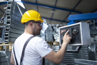 pracownik fabryki obslugujacy maszyne przemyslowa i ustawiajacy parametry na komputerze Jak wybrać odpowiedniego producenta maszyn przemysłowych dla Twojego biznesu
